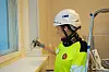 Maler i vernet bygg påfører maling rundt vindu iført hjelm og verneutstyr.