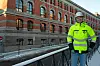 Bygningsarbeider i gul jakke og hjelm foran stort murbygg en vinterdag.
