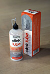 Flaske og eske med Click Lube smøremiddel plassert på et parkettgulv.
