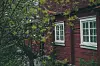 Rødt, eldre våningshus i tre delvis skjult bak grønne trær.