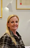 Kvinne i rutete skjorte sitter innendørs og ser mot kamera med et smil.