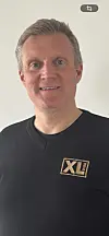 Person i svart genser med XL-BYGG-logo foran lys vegg.