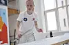 Ung maler i hvite arbeidsklær påfører mønster på en stor dekorert flate i et lyst rom.